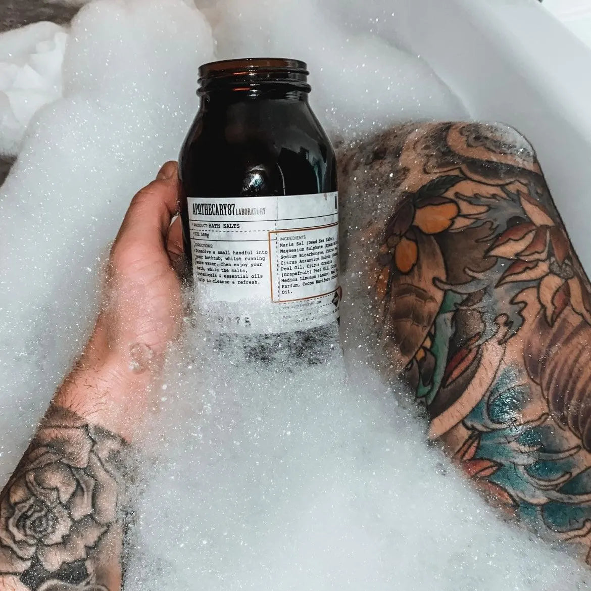 Apothecary 87 cleansing Bath Salts in bath held by tattooed person